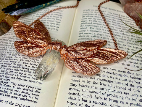copper fairy wing necklace on a book surrounded by crystals and air plants